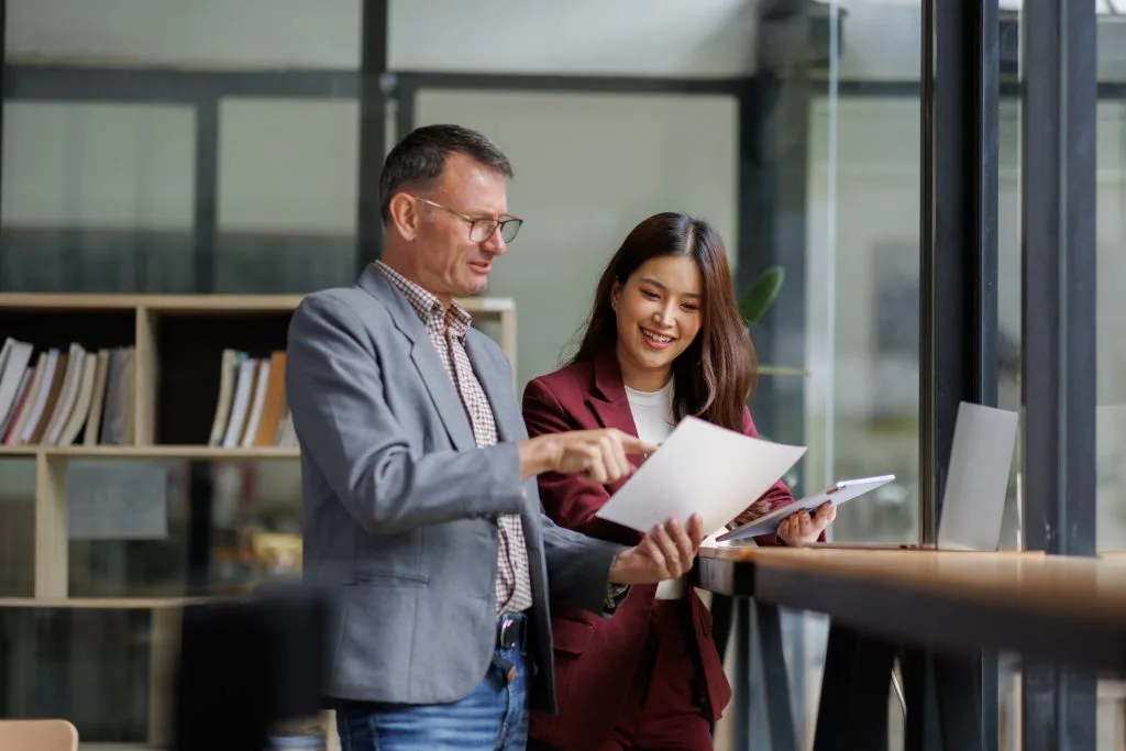 A man and a woman discussing documents in a modern office, emphasizing their collaboration about us