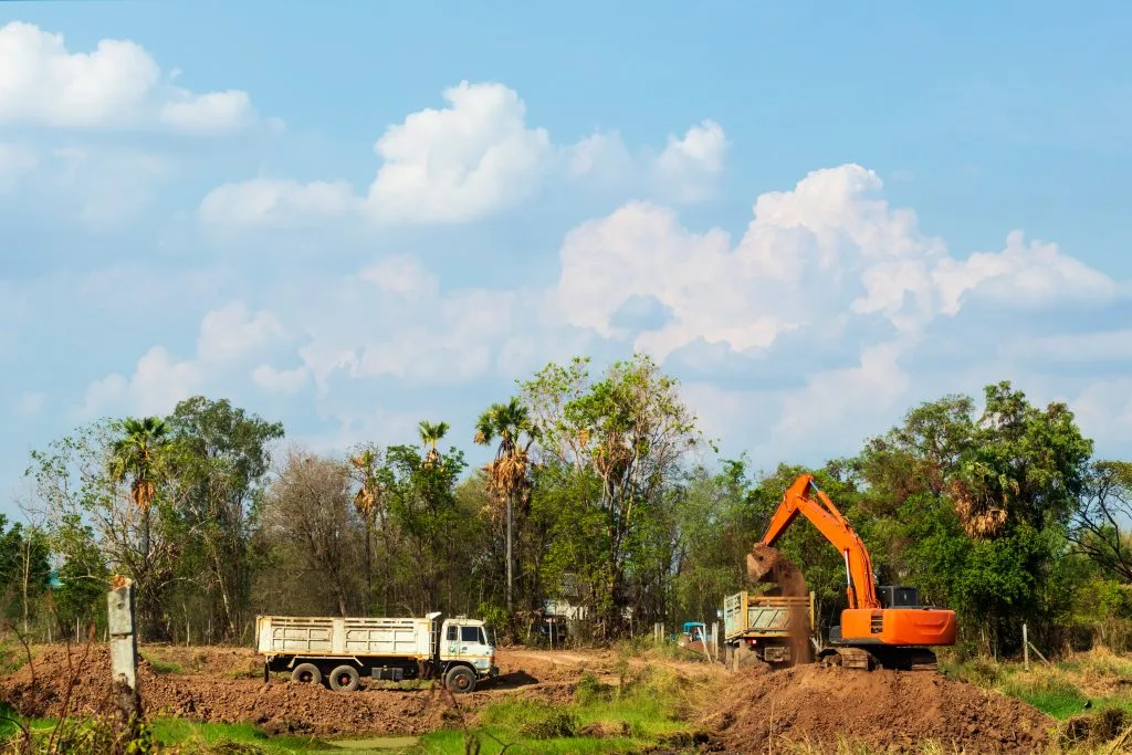 Land servicing involves an excavator digging at a construction site with a waiting truck nearby