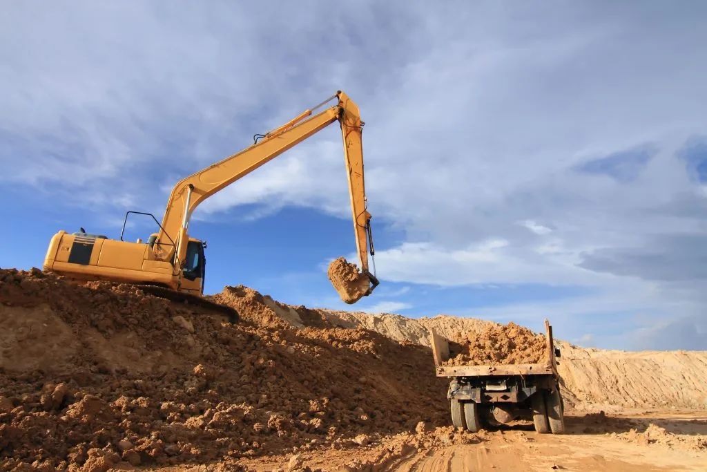 Land servicing involves an excavator lifting dirt for a waiting truck to load