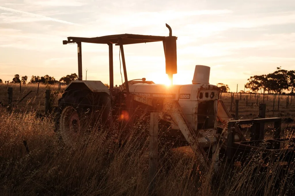 A tractor sits in tall grass as the sun sets behind it